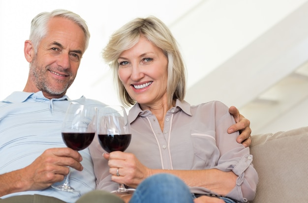 Souriant couple d&#39;âge mûr avec des verres à vin assis sur le canapé