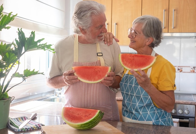 Souriant couple caucasien senior dans la cuisine à domicile tenant une tranche de pastèque fraîche rouge tout en se regardant régime de fraîcheur d'hydratation et concept de saine alimentation