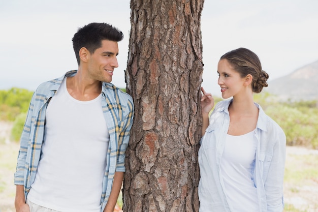 Souriant couple debout par un tronc d&#39;arbre