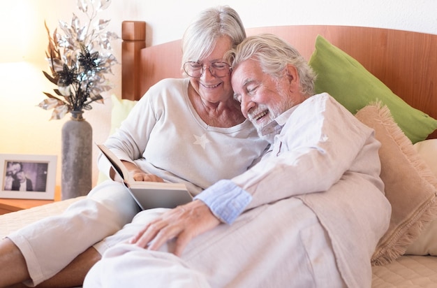 Souriant couple de famille senior ensemble au lit en lisant un livre homme et femme caucasiens âgés se relaxant