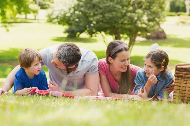 Souriant couple avec jeunes enfants couché sur l&#39;herbe dans le parc