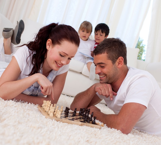 Souriant couple jouant aux échecs sur le sol dans le salon