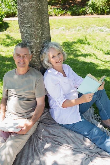 Photo souriant couple mature assis contre l'arbre au parc