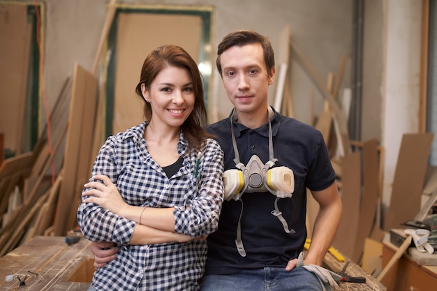 Souriant couple menuisiers assis en atelier sur fond de planches