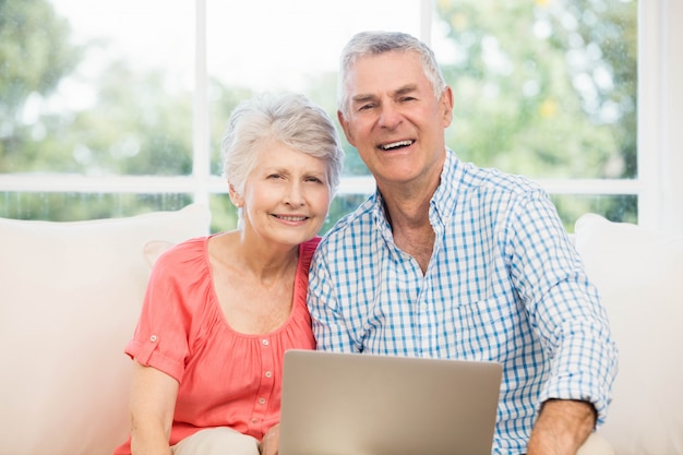 Souriant couple de personnes âgées à l'aide d'un ordinateur portable sur le canapé