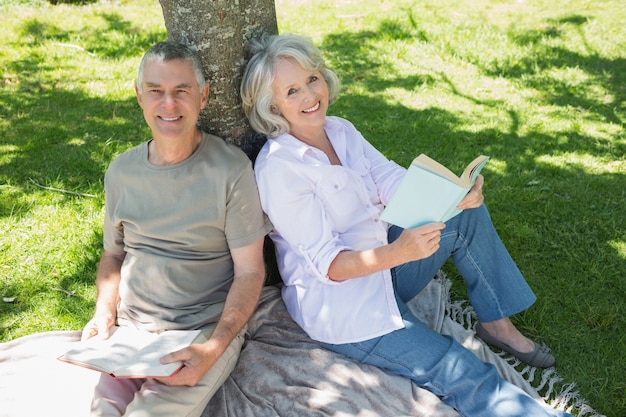 souriant couple senior assis contre l&#39;arbre au parc