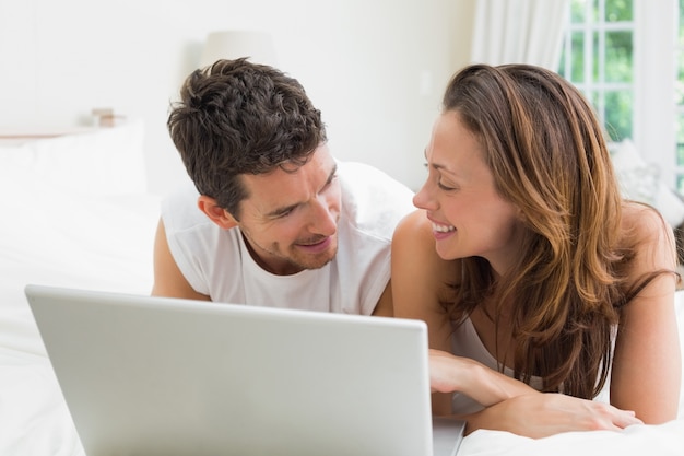 Souriant couple utilisant un ordinateur portable dans son lit