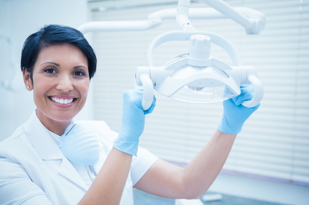 Souriant dentiste femme ajustant la lumière