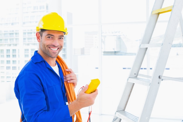 Souriant électricien mâle tenant multimètre au bureau