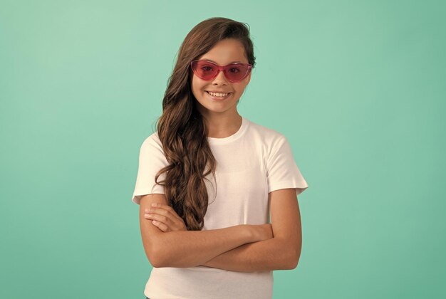 Souriant enfant long cheveux bouclés dans un style décontracté de lunettes de soleil sur l'accessoire de mode de fond bleu