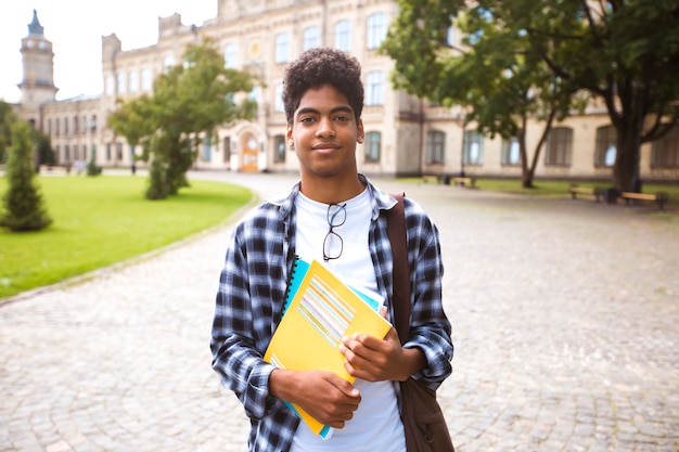 Souriant étudiant afro-américain à lunettes avec des livres.