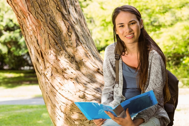 Souriant étudiant assis sur le tronc et tenant un livre