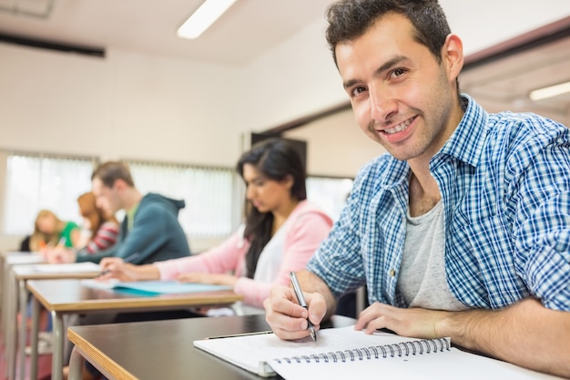 Souriant étudiant avec d&#39;autres personnes écrivant des notes dans la salle de classe