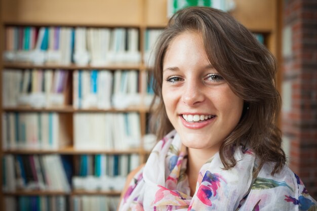 Souriant étudiante contre l&#39;étagère de la bibliothèque