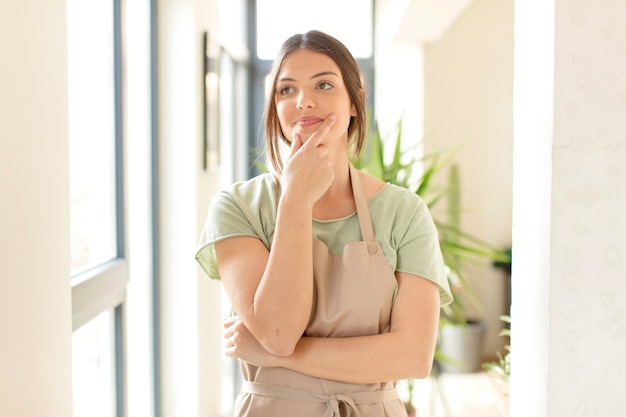 souriant avec une expression heureuse et confiante avec la main sur le menton, se demandant et regardant sur le côté