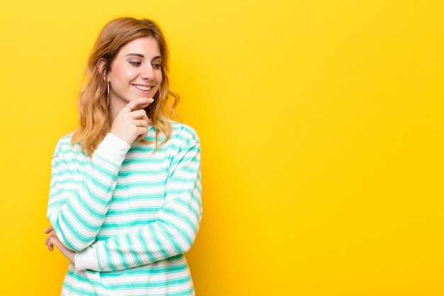 souriant avec une expression heureuse et confiante avec la main sur le menton, se demandant et regardant de côté