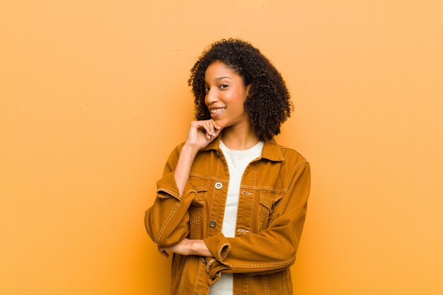 souriant avec une expression heureuse et confiante avec la main sur le menton, se demandant et regardant de côté