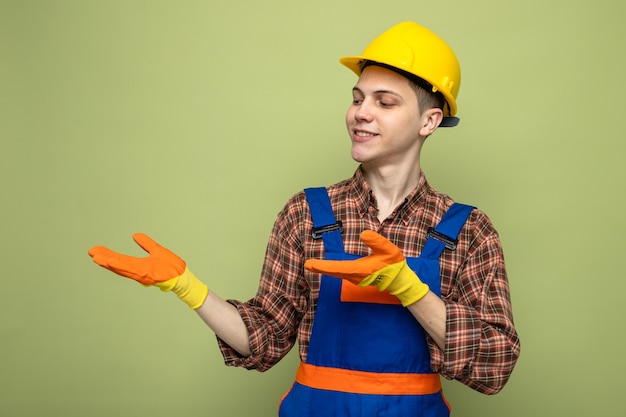 Souriant faisant semblant de tenir et de pointer avec la main quelque chose de jeune constructeur masculin portant un uniforme avec des gants