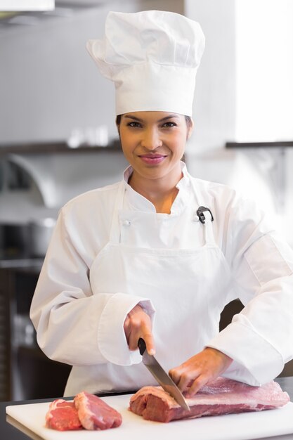 Souriant femme chef coupe viande dans la cuisine