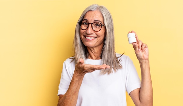 Souriant gaiement, se sentant heureux et montrant un concept dans l'espace de copie avec la paume de la main et tenant une bouteille de pilules