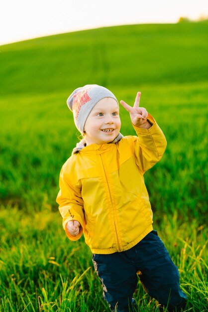 Souriant garçon d'âge préscolaire caucasien montre le geste de la victoire à l'extérieur