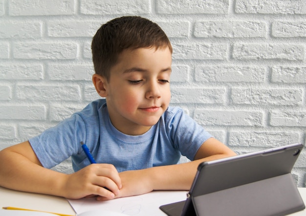 Souriant garçon enfant européen en t-shirt bleu utilise un ordinateur portable et communique sur Internet à la maison. École à la maison, apprentissage à distance, éducation en ligne, appel vidéo