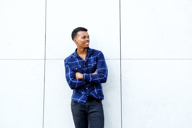 Souriant homme africain debout avec les bras croisés contre le mur