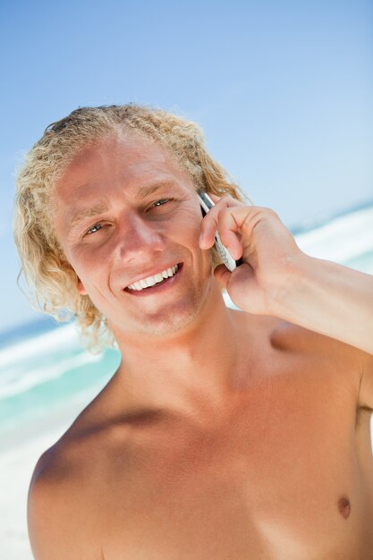 Souriant homme blond en regardant la caméra tout en appelant avec son téléphone portable