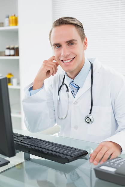 Souriant homme médecin assis avec un ordinateur au cabinet médical