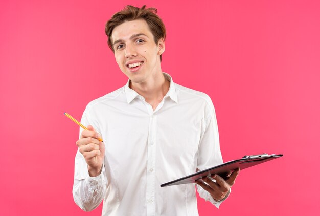 Souriant Jeune Beau Mec Vêtu D'une Chemise Blanche Tenant Un Presse-papiers Avec Un Stylo Isolé Sur Un Mur Rose