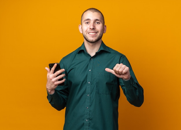 Souriant jeune beau mec vêtu d'une chemise verte tenant et pointe au téléphone