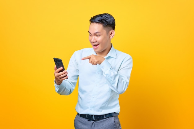Souriant jeune bel homme d'affaires pointant sur smartphone sur fond jaune