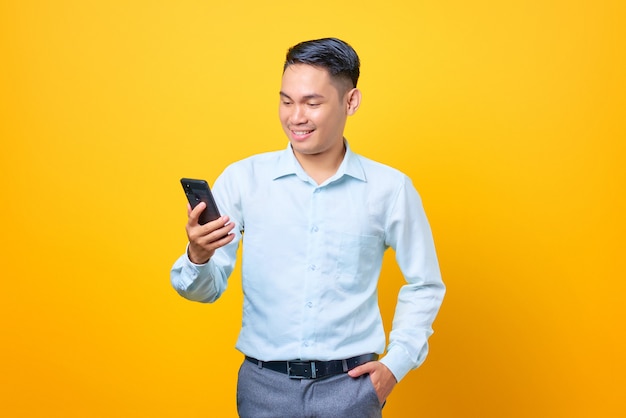 Souriant jeune bel homme d'affaires regardant l'écran du téléphone portable sur fond jaune