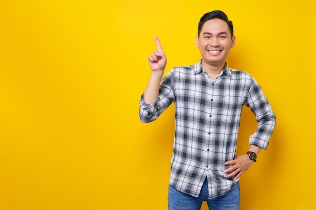 Souriant jeune bel homme asiatique vêtu d'une chemise à carreaux pointant les doigts de côté sur un espace vide pour le texte publicitaire isolé sur fond jaune Concept de style de vie des gens