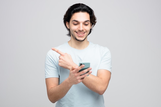 souriant jeune bel homme utilisant un téléphone portable pointant vers le côté isolé sur fond blanc