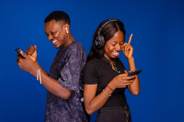 Souriant jeune couple amis homme femme dans des vêtements décontractés debout dos à dos à l'aide de téléphones portables