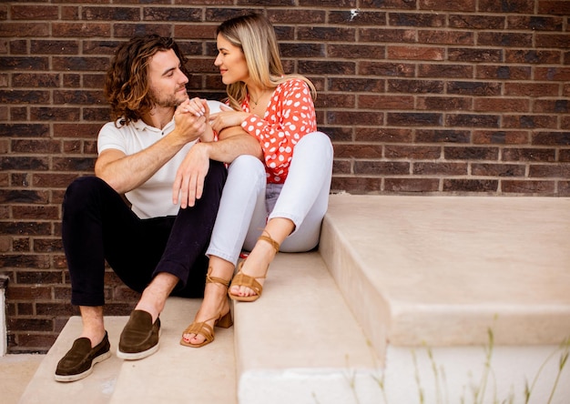 Souriant jeune couple amoureux assis devant le mur de briques de la maison