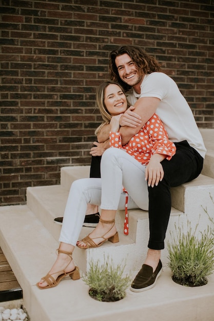 Souriant jeune couple amoureux devant le mur de briques de la maison