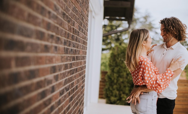 Souriant jeune couple amoureux devant le mur de briques de la maison