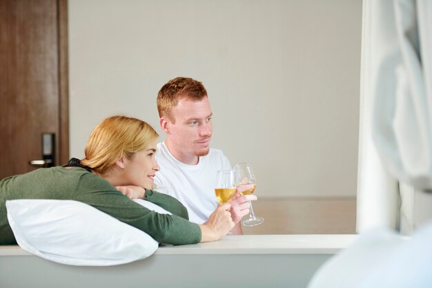 Souriant jeune couple buvant du champagne et regardant un film ou une émission de télévision