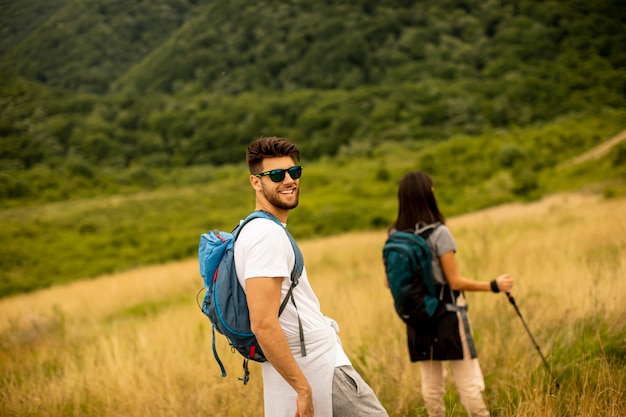 Souriant jeune couple marchant avec des sacs à dos sur les collines verdoyantes