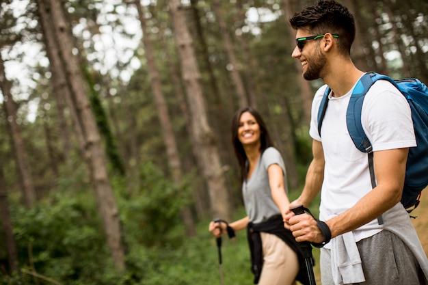 Souriant jeune couple marchant avec des sacs à dos dans la forêt un jour d'été