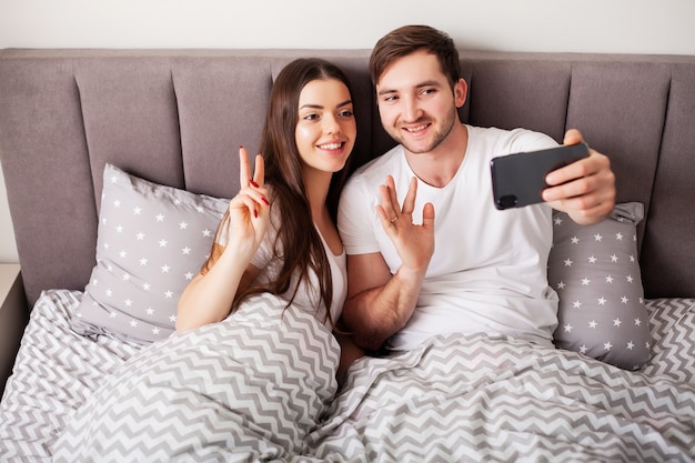 Souriant jeune couple prenant selfie ensemble dans la chambre