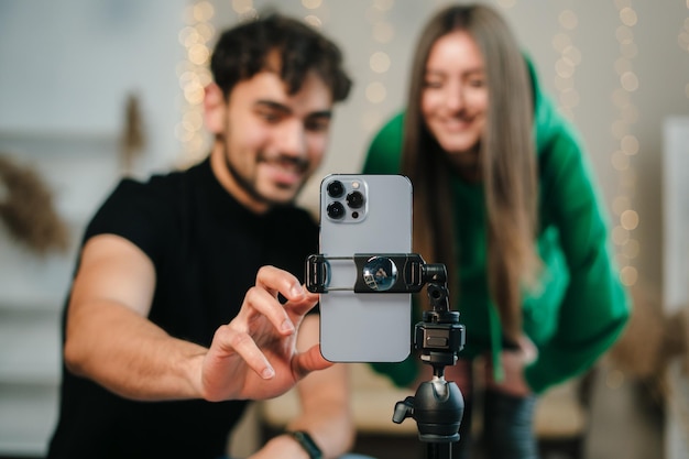 Souriant jeune couple avec des visages heureux regardant les blogueurs de l'appareil photo du téléphone enregistrant un vidéoblog à la maison Vidéo en direct