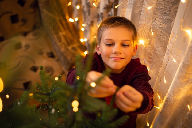 Souriant jeune garçon décorant l'arbre de Noël dans la salle pleine de lumières, vue d'en haut.