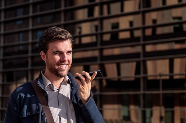 Souriant jeune homme d'affaires envoyant un message vocal