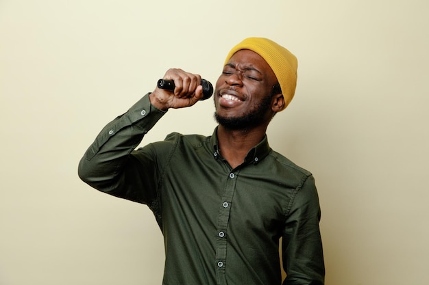 Souriant jeune homme afro-américain en chapeau portant une chemise verte parle sur haut-parleur isolé sur fond blanc