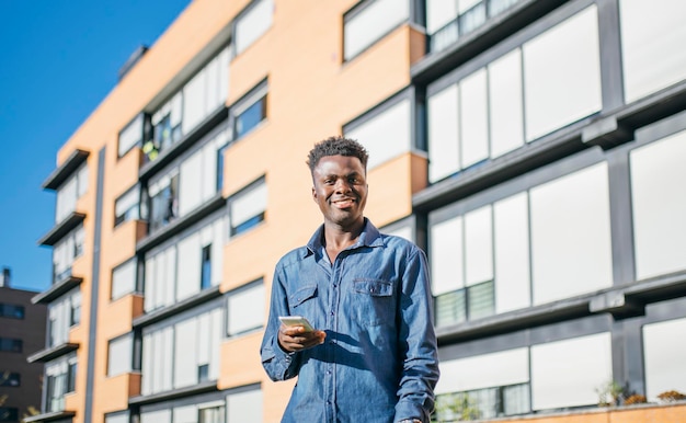 Souriant jeune homme afro-américain tenant un smartphone par une journée ensoleillée en ville ou en zone urbaine