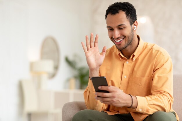 Souriant jeune homme agitant la main à l'aide de téléphone portable