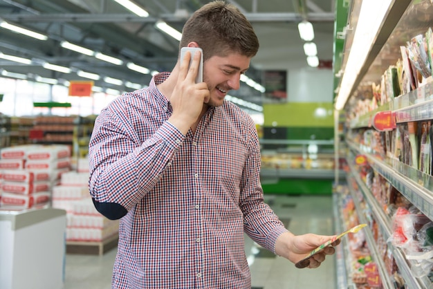 Souriant jeune homme à l'aide de téléphone portable tout en faisant du shopping dans un magasin